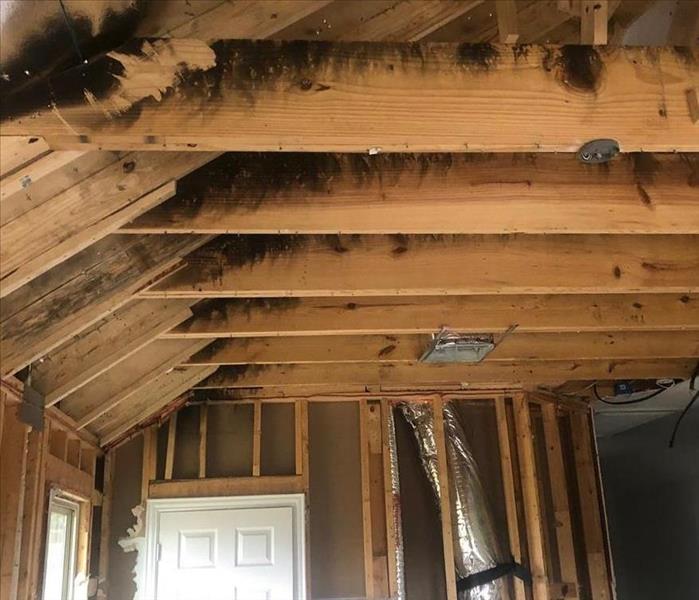 Exposed wooden beams in ceiling with fire damage and soot